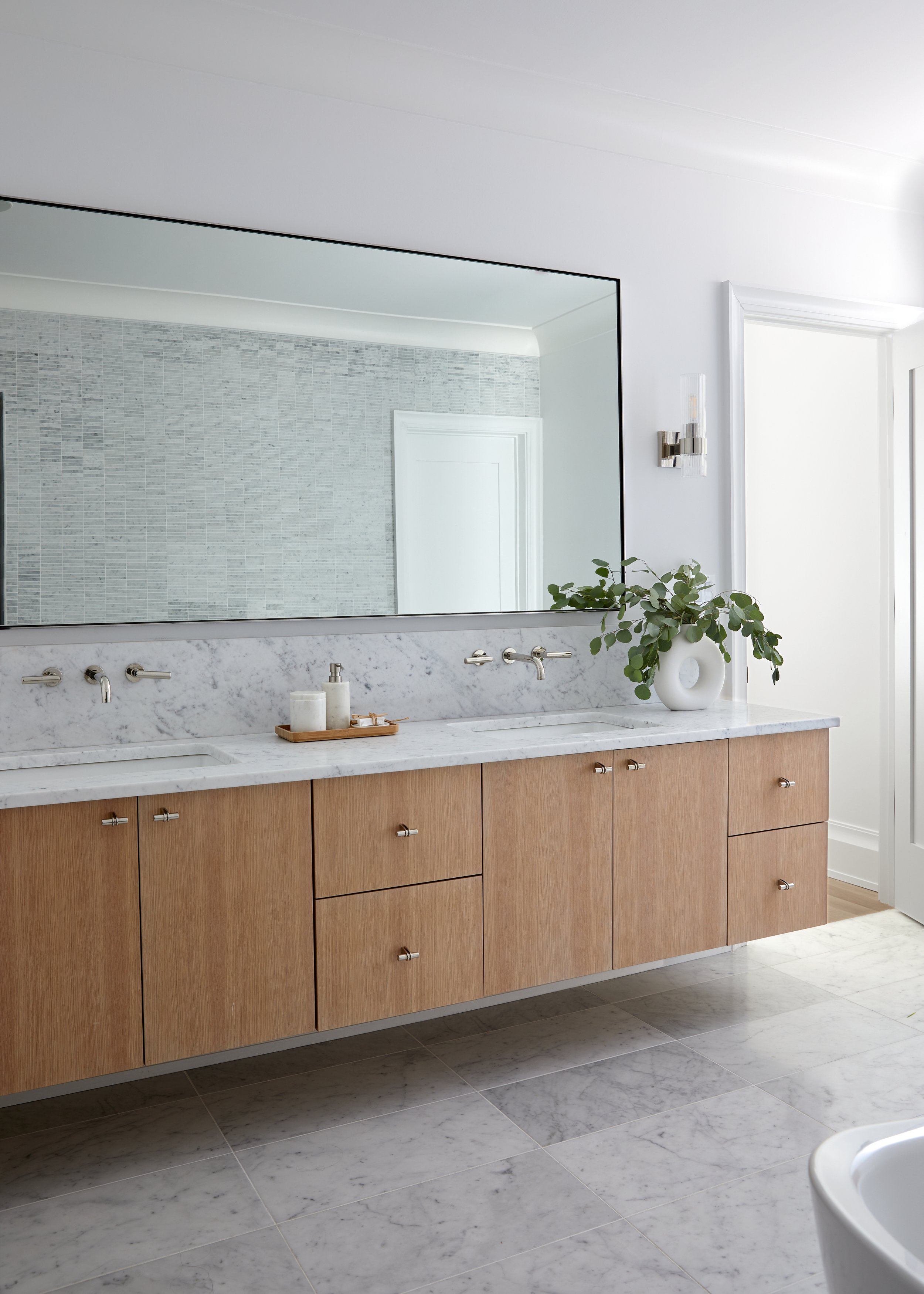 Primary bathroom double vanity in Westfield, New Jersey with white oak flat-panel cabinets, a marble countertop and backsplash and wall-mounted polished nickel faucets by Ellie Mroz Design.