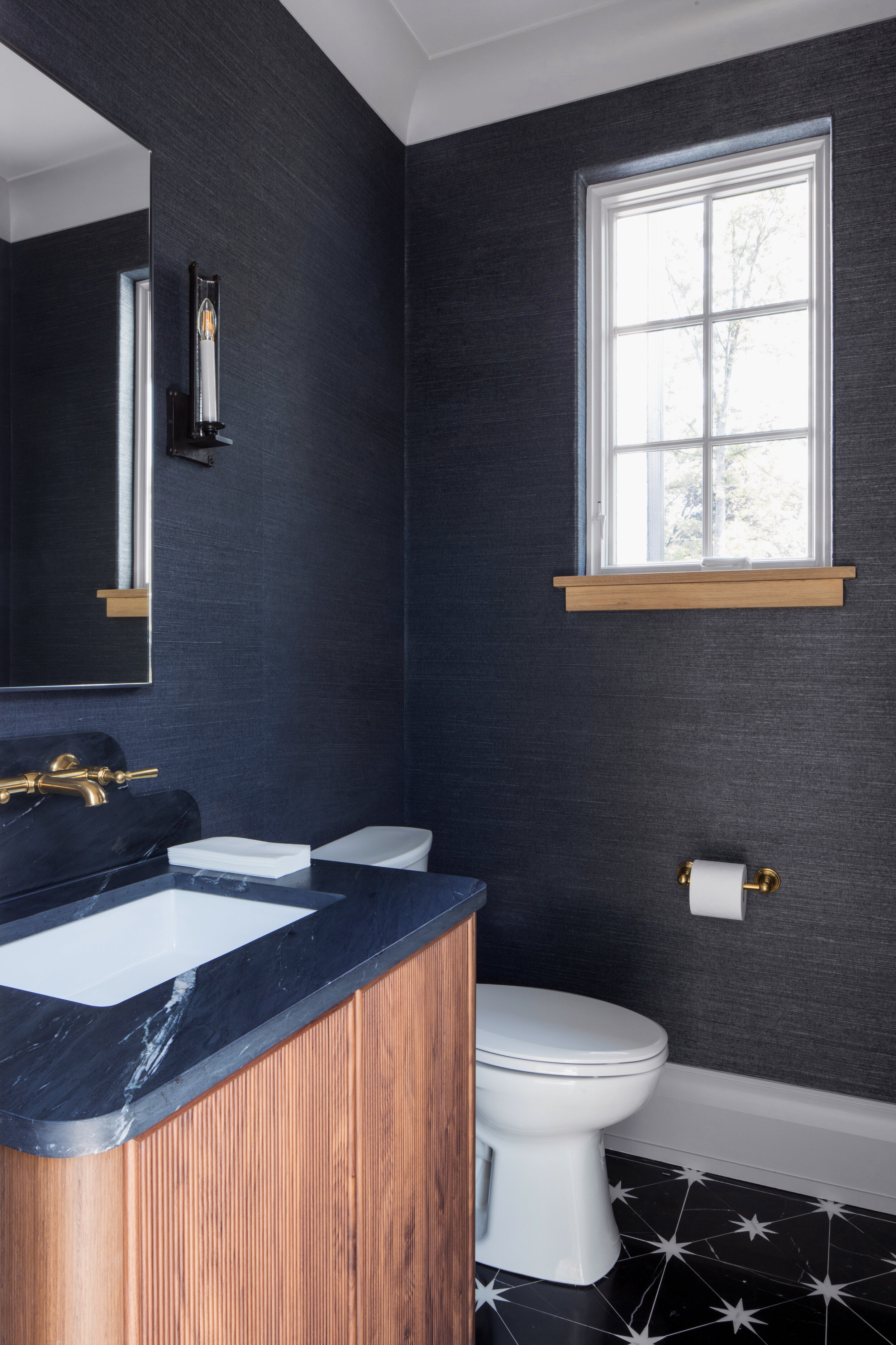 Powder room in navy grasscloth with a black tile floor in a Westfield, New Jersey custom home by Ellie Mroz Design.