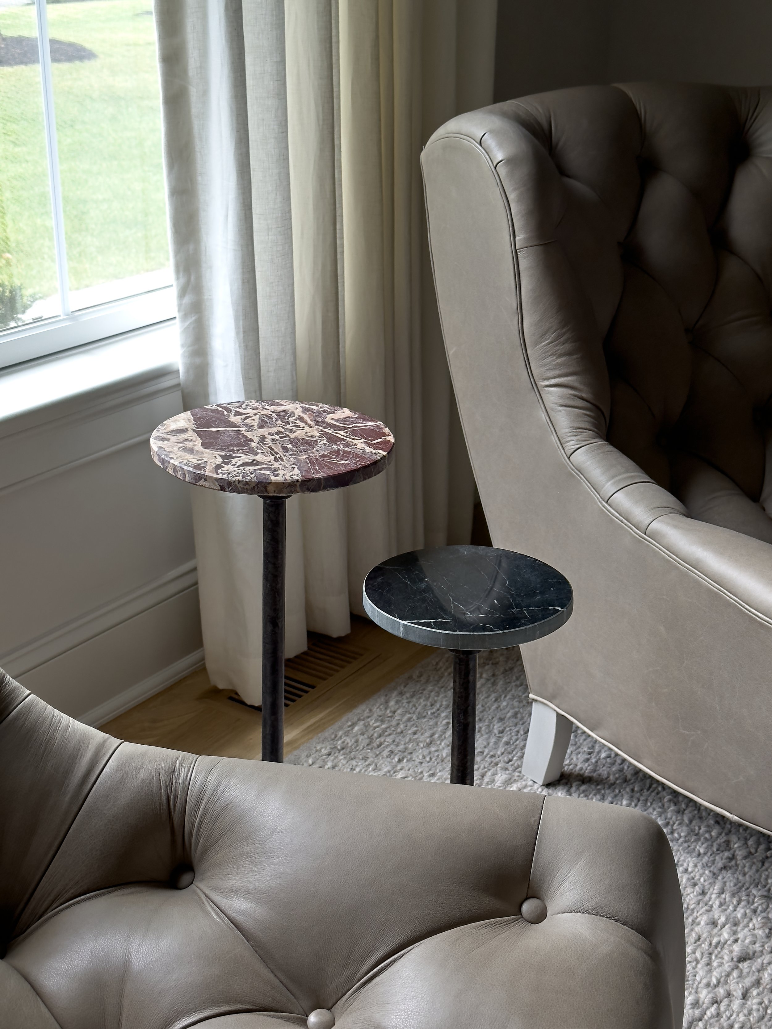 Marble-top pedestal side tables between leather chairs in a Chatham, NJ living room by Ellie Mroz Design.