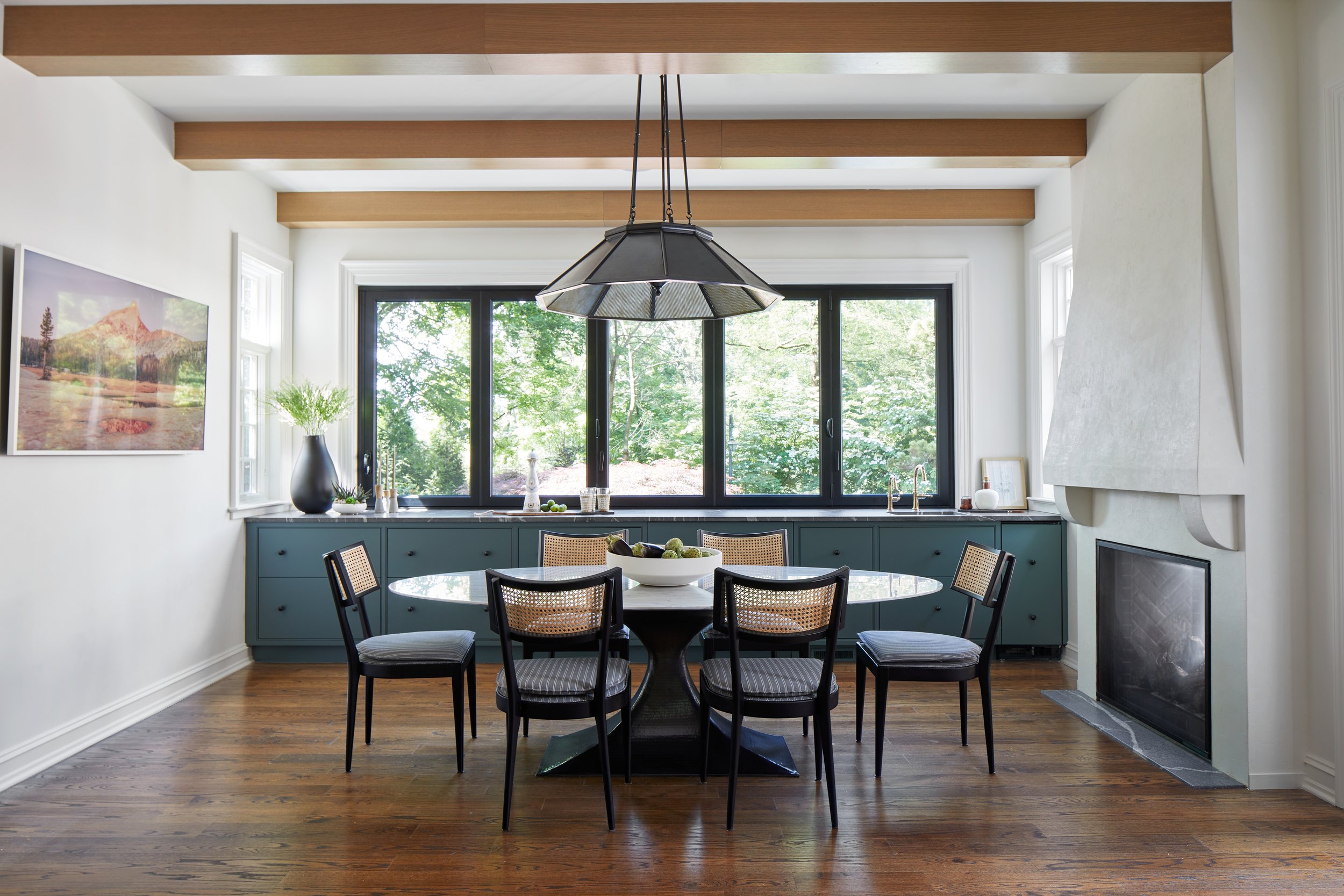 Breakfast room with cane-back chairs, oak ceiling beams and a two-sided fireplace in a Westfield, New Jersey 1929 home renovation by Ellie Mroz Design.