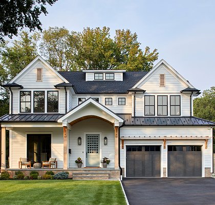 White modern farmhouse exterior with twin gables, black-framed windows, a standing-seam porch roof, arched portico entry and a two-car garage, in New Jersey by Ellie Mroz Design.