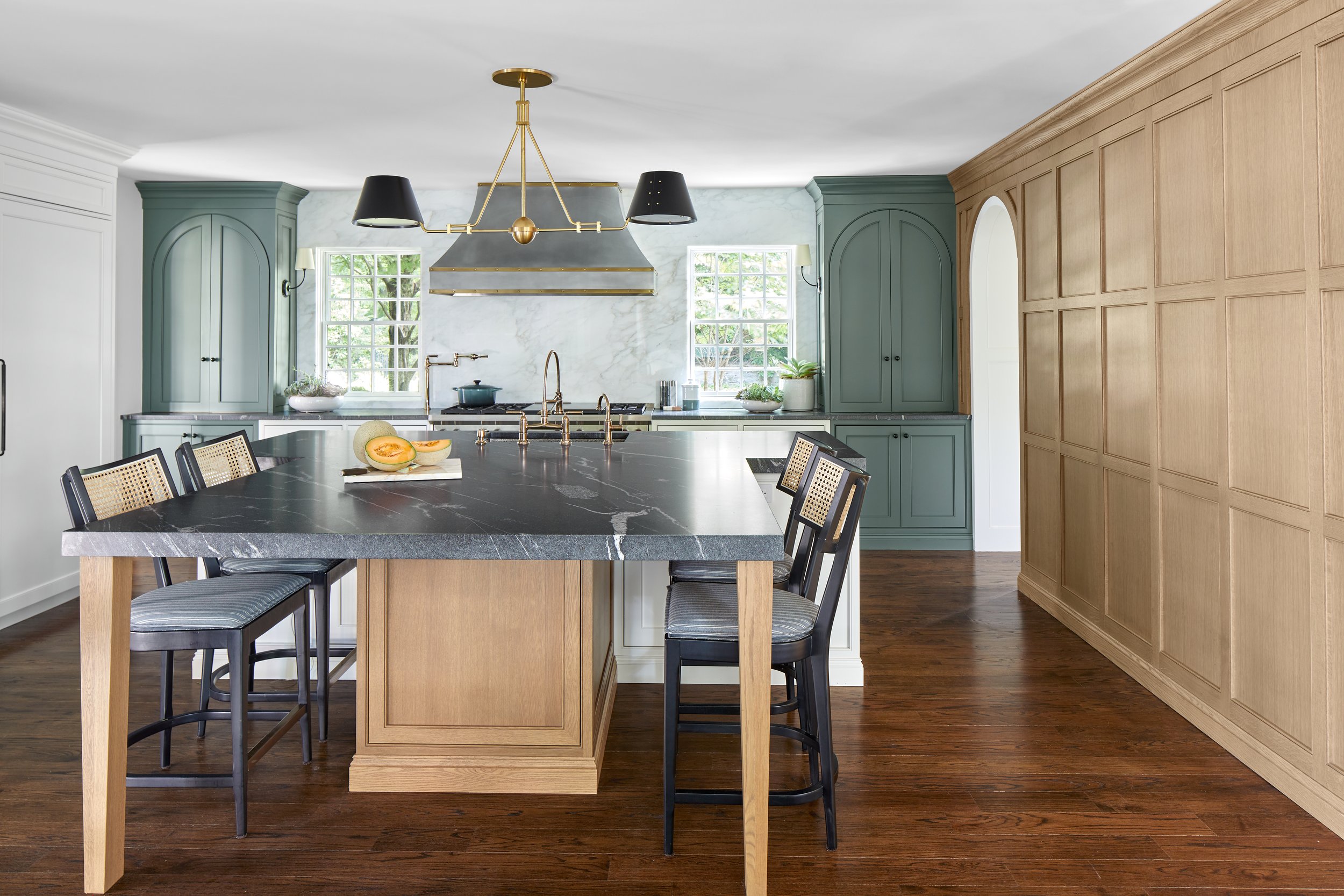 Kitchen with sage green cabinetry, arched upper cabinets and a soapstone-topped island with cane-back stools in a Westfield, New Jersey 1929 home renovation by Ellie Mroz Design.