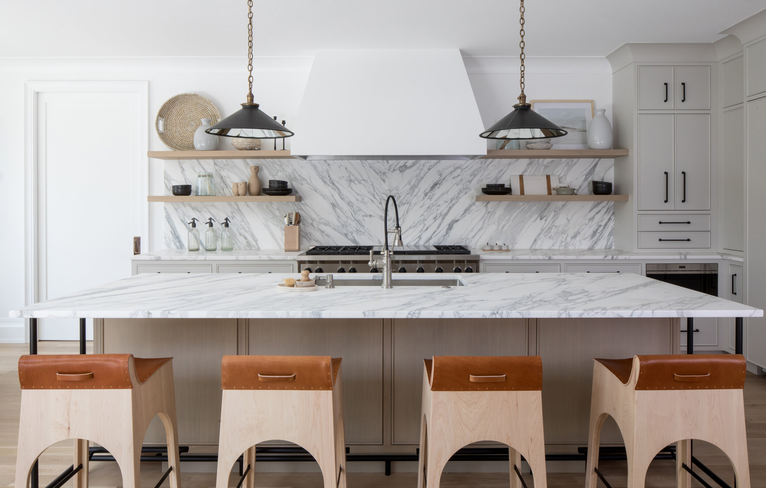Marble-topped island with leather counter stools and a marble slab backsplash in a Westfield, New Jersey custom kitchen by Ellie Mroz Design.