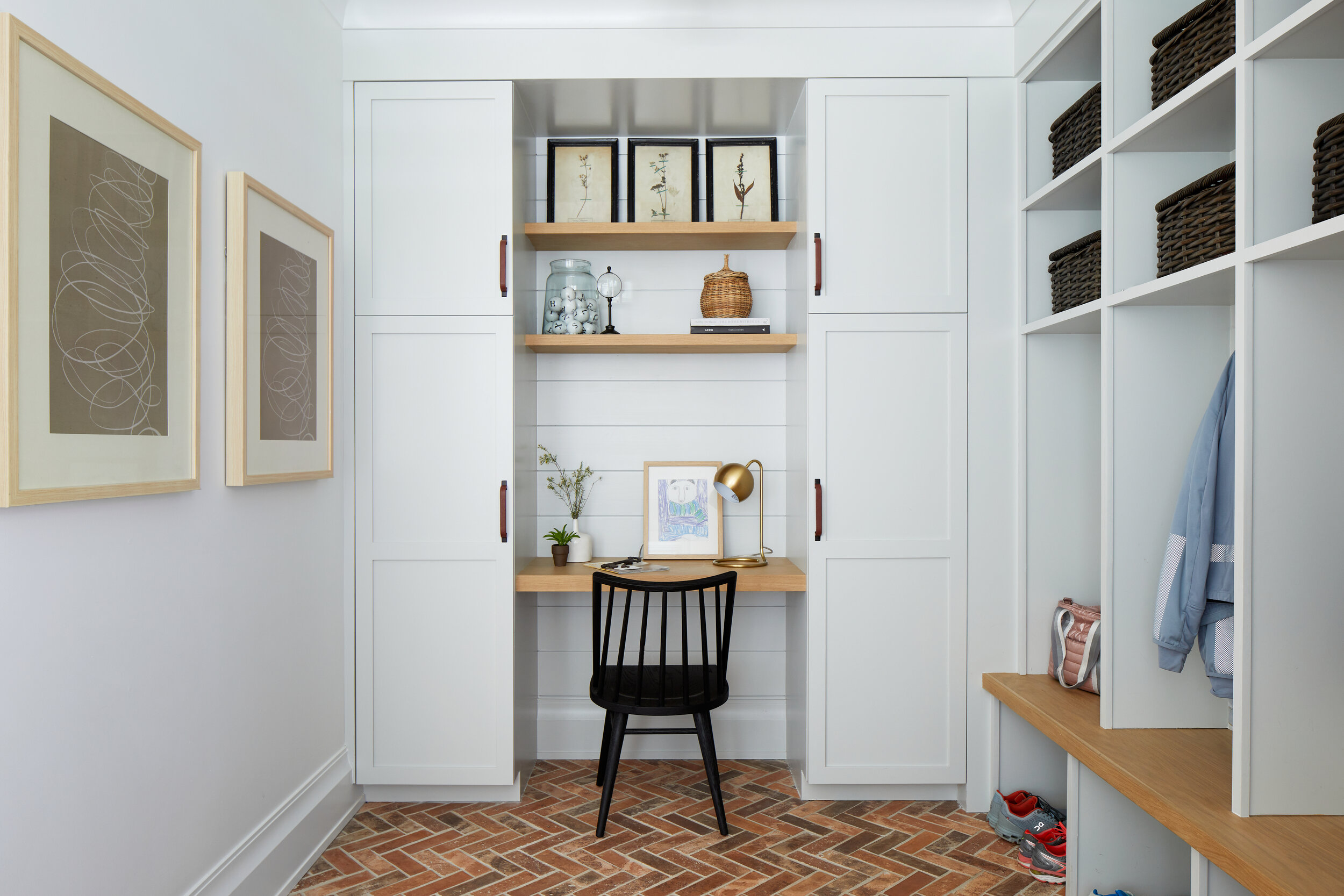 Mudroom with white built-in cubbies, a small desk nook with a black spindle chair and a herringbone brick floor in a Westfield, New Jersey modern farmhouse by Ellie Mroz Design.