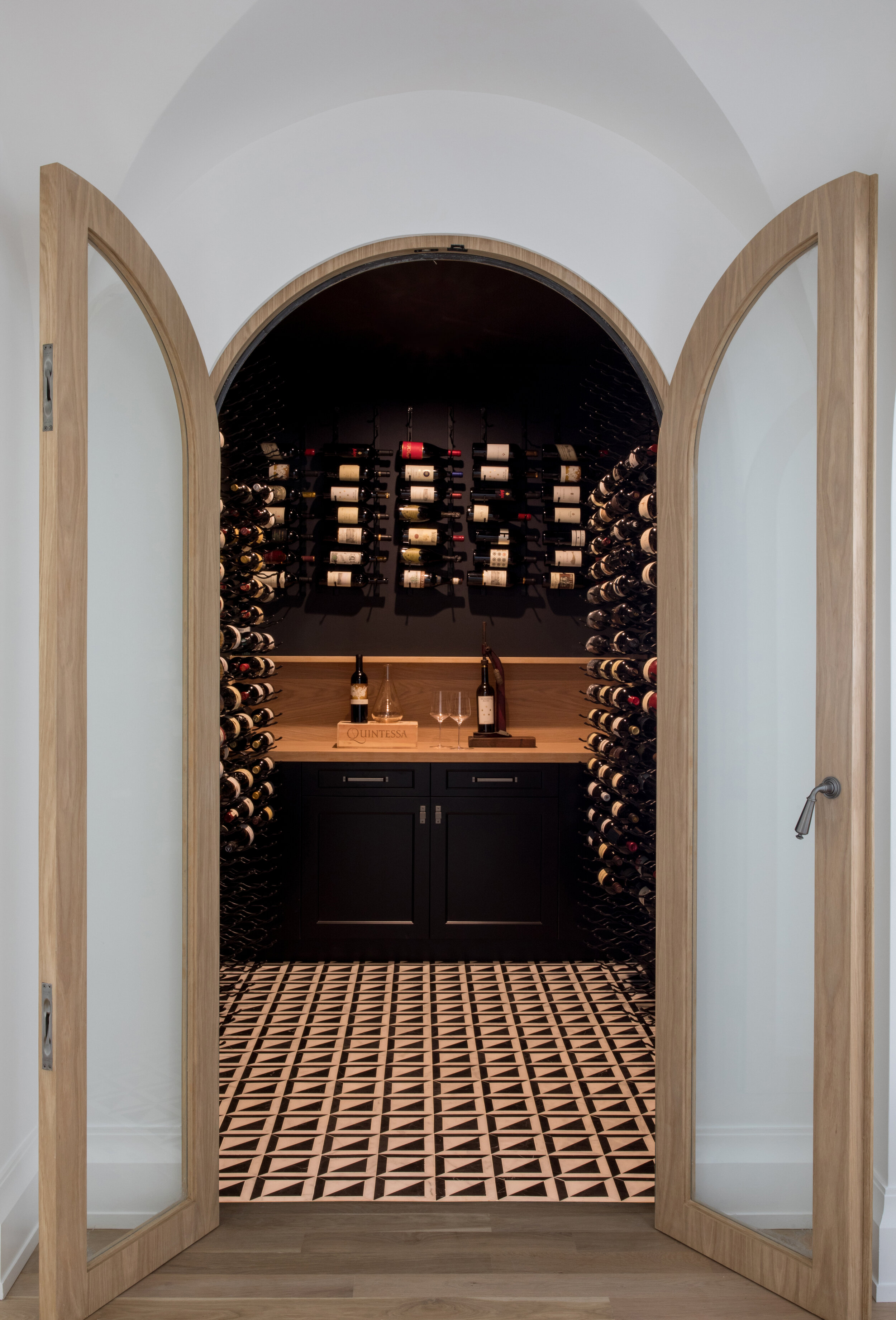 Home wine cellar with arched doors and full-height wall racks in a Westfield, New Jersey home by Ellie Mroz Design.